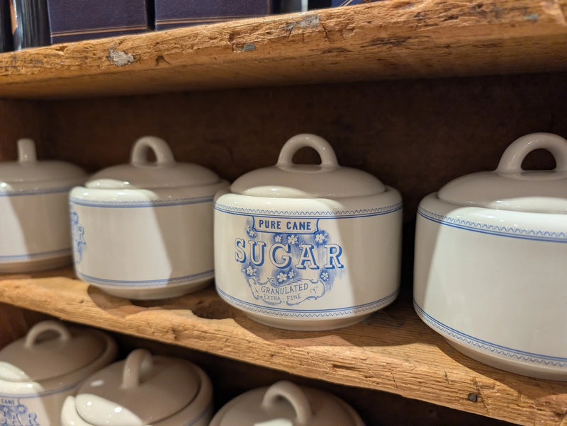 Close-up of lidded Pure Cane Sugar bowls on a rustic wooden shelf
