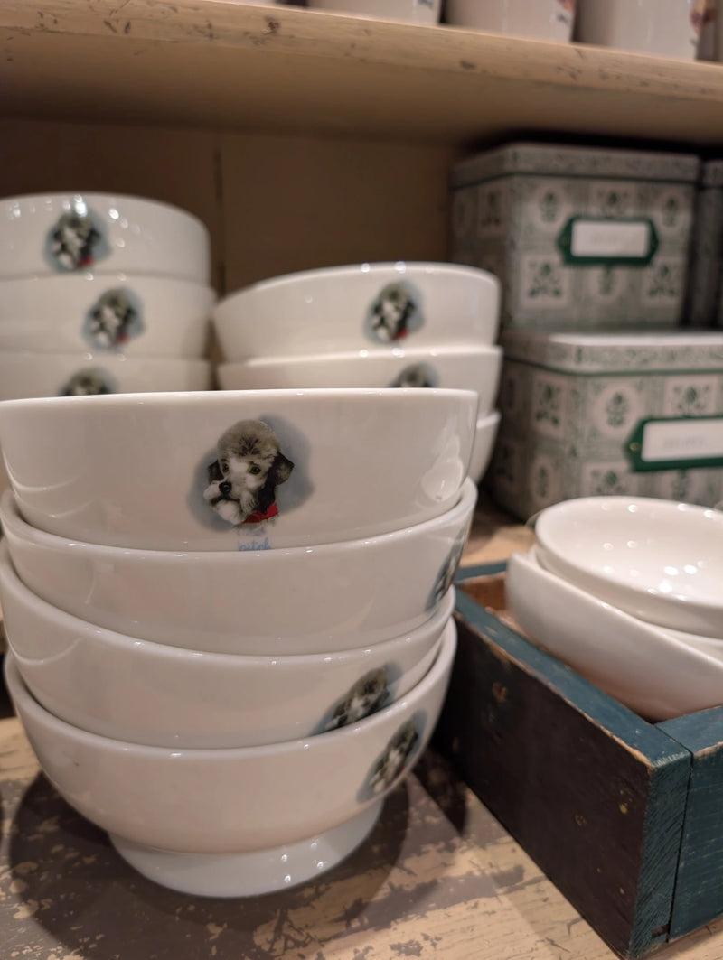 Stacked cream footed pet bowls with a small dog portrait on a store shelf